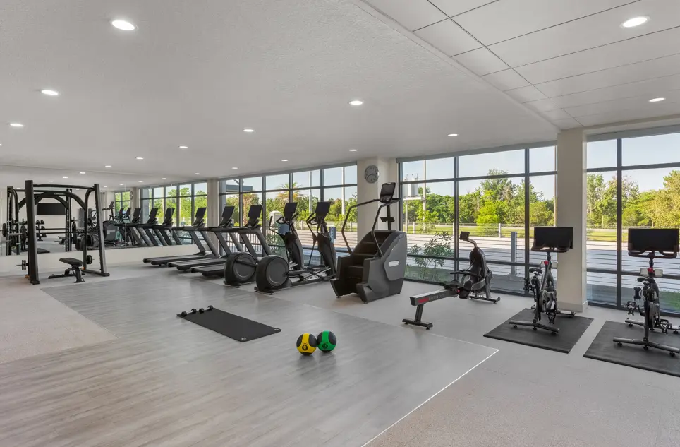 EVEN Hotel's fitness center featuring treadmills, stationary bikes, stair climbers, and resistance training equipment, with floor-to-ceiling windows offering scenic views of surrounding greenery.