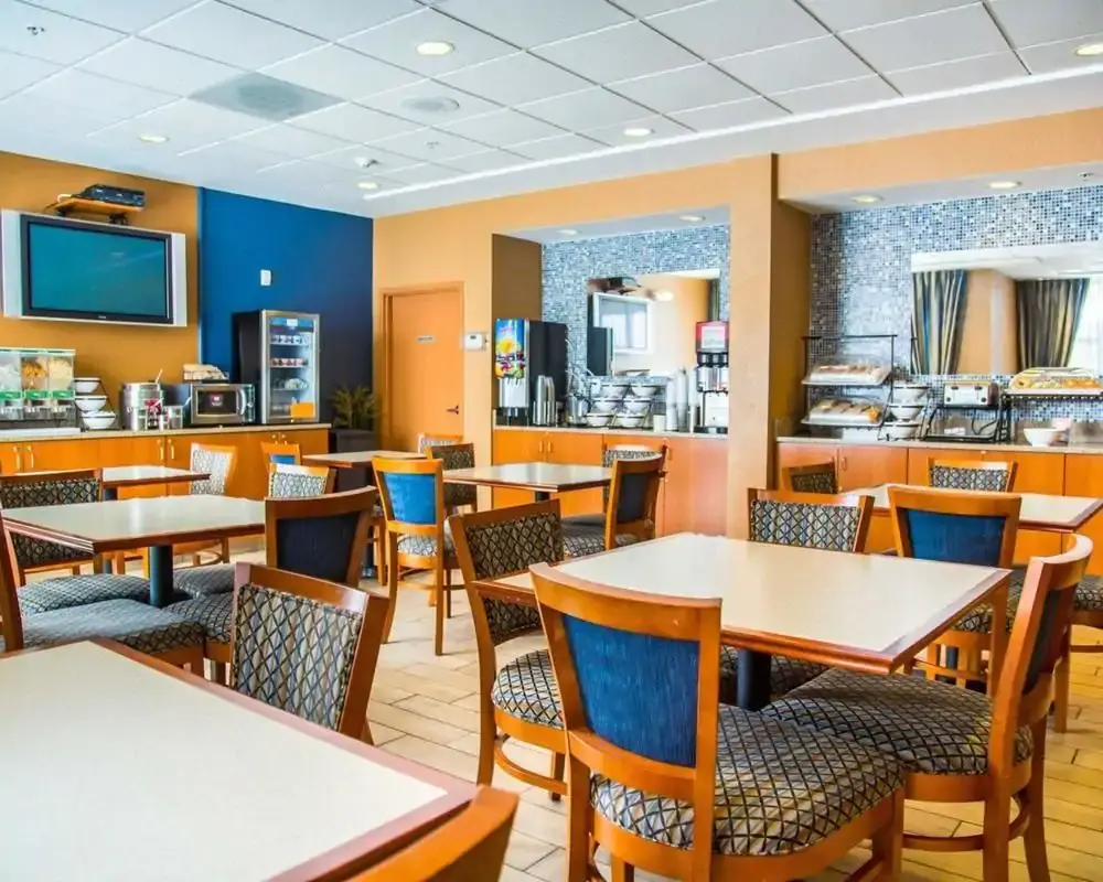 Comfort Inn & Suites dining area with tables and chairs, featuring a breakfast buffet with various food items and beverages.