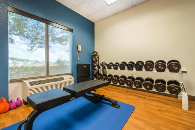Fitness center at Comfort Inn & Suites with a bench, a rack of dumbbells, and large windows providing natural light.