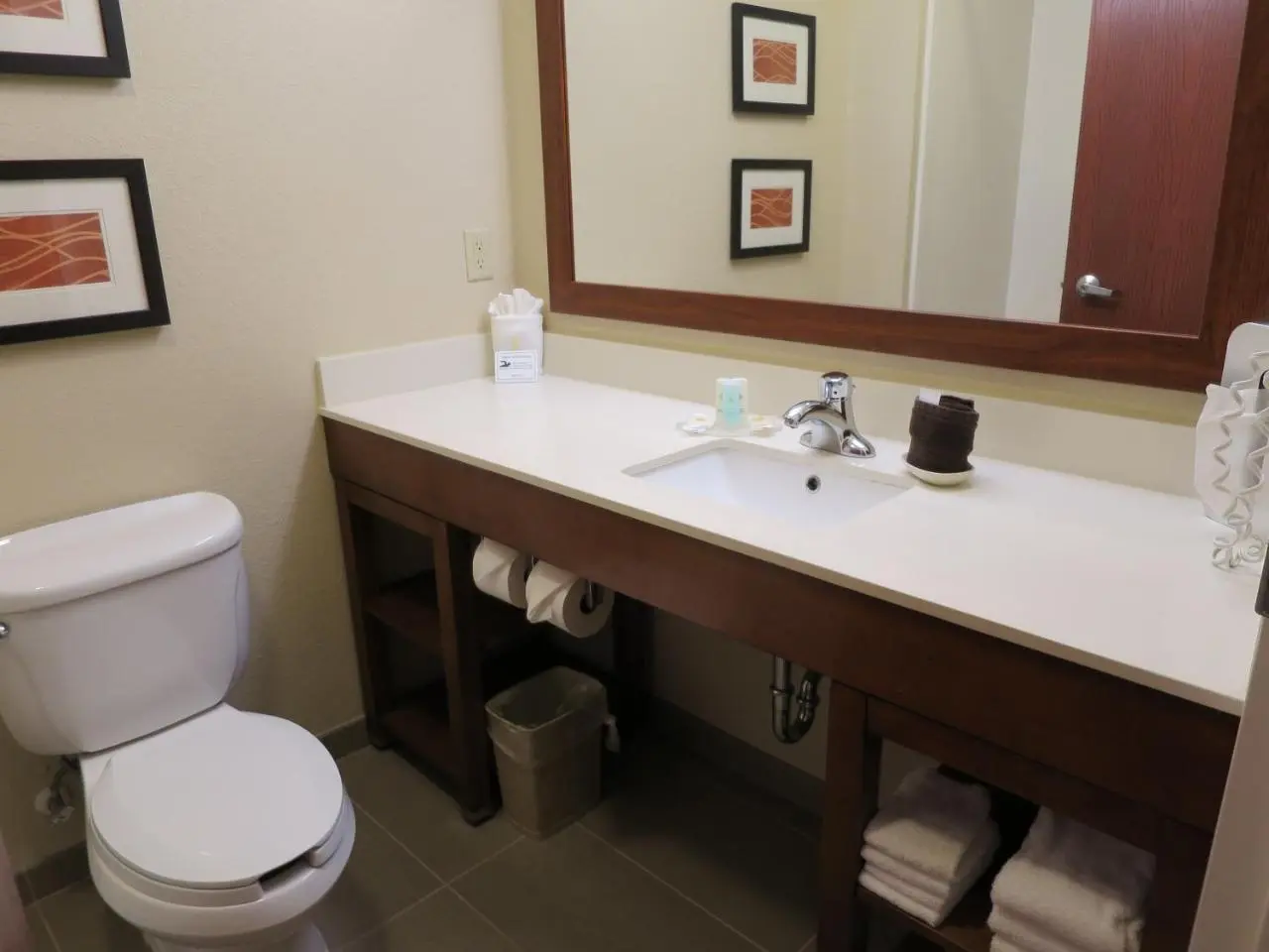 Modern bathroom at Comfort Inn & Suites featuring a toilet, wide vanity with a large mirror, and open shelves.