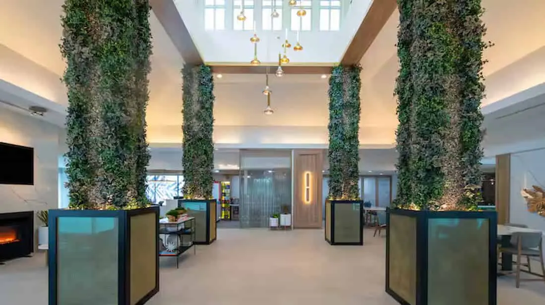 Spacious and modern lobby of Hilton Garden Inn Orlando Airport featuring tall greenery-covered columns, contemporary lighting fixtures, and stylish seating areas with a welcoming, open design.