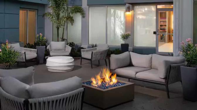 Evening view of a courtyard at the Hilton Garden Inn Orlando Airport Hotel with comfortable wicker seating and a central fire pit surrounded by lush greenery.