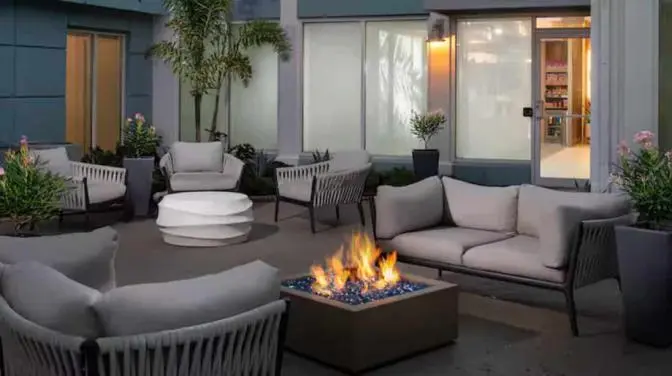 Evening view of a courtyard at the Hilton Garden Inn Orlando Airport Hotel with comfortable wicker seating and a central fire pit surrounded by lush greenery.