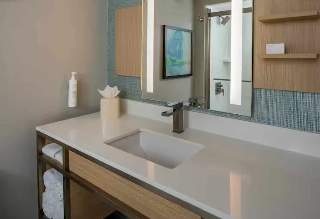 Modern guest bathroom at Hilton Garden Inn Orlando Airport featuring a sleek vanity with a wide mirror, contemporary lighting, and minimalist wood accents.