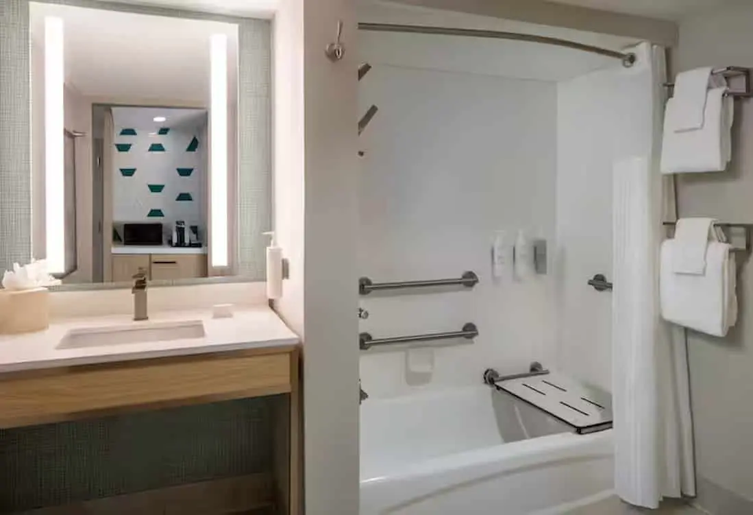 Bathroom designed for accessibility, including a granite sink area, a large mirror, and a walk-in shower with safety bars and a bench.