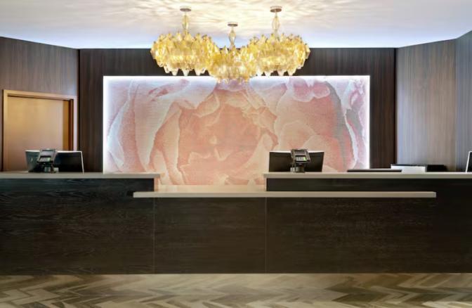 Front desk at DoubleTree by Hilton Hotel Orlando East-UCF Area featuring a modern reception counter with dark wood finishes, a floral accent wall, and elegant golden chandeliers above.