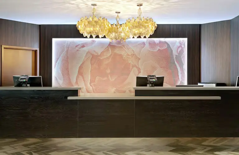 Front desk at DoubleTree by Hilton Hotel Orlando East-UCF Area featuring a modern reception counter with dark wood finishes, a floral accent wall, and elegant golden chandeliers above.
