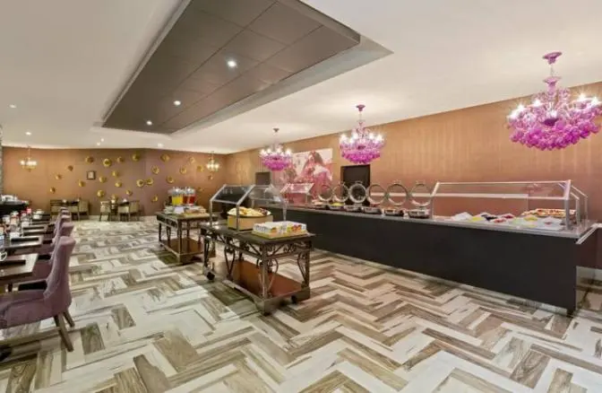 Breakfast area at DoubleTree by Hilton Hotel Orlando East-UCF Area featuring a modern buffet setup with hot and cold selections, elegant purple chandeliers, and contemporary dining tables with upholstered chairs.