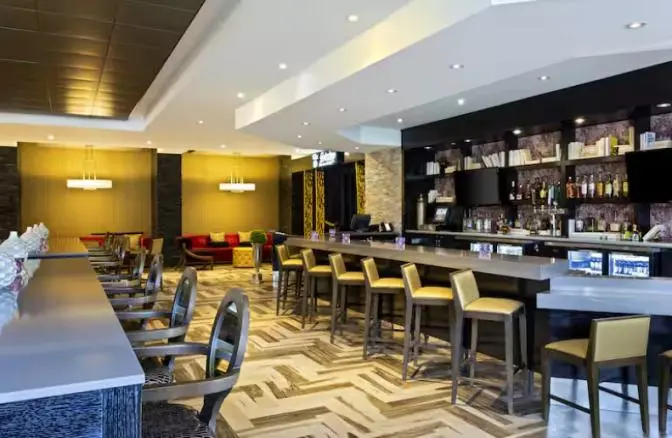 Stylish bar and lounge area at DoubleTree by Hilton Hotel Orlando East-UCF Area featuring a sleek bar counter with high-top seating, warm gold lighting, and a cozy seating area with modern decor.