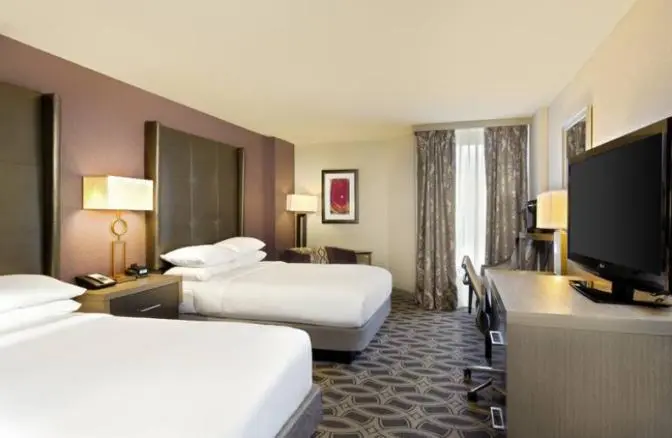 Double queen guest room at DoubleTree by Hilton Hotel Orlando East-UCF Area featuring two plush beds with tufted headboards, a work desk with a flat-screen TV, and warm contemporary lighting for a comfortable stay.