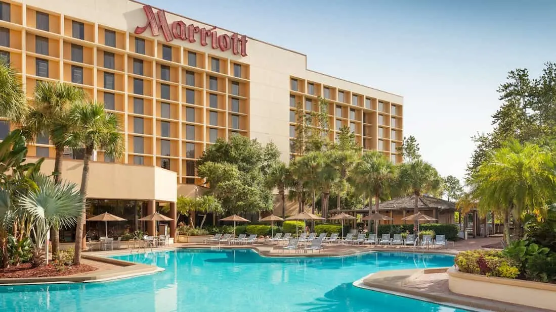 Marriott Lakeside Orlando International Airport Hotel exterior with a large pool, palm trees, and sunbathing areas under umbrellas.