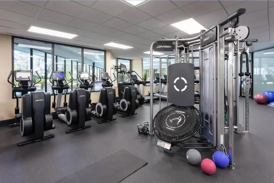 Modern gym with multiple elliptical machines, a treadmill, and diverse workout equipment including a trampoline and kettlebells.