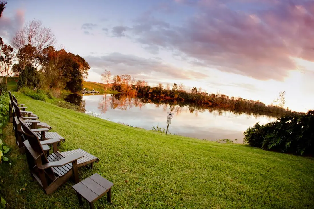 Peaceful lakeside setting at Marriott Lakeside with Adirondack chairs arranged along the grassy bank, overlooking the sunset
