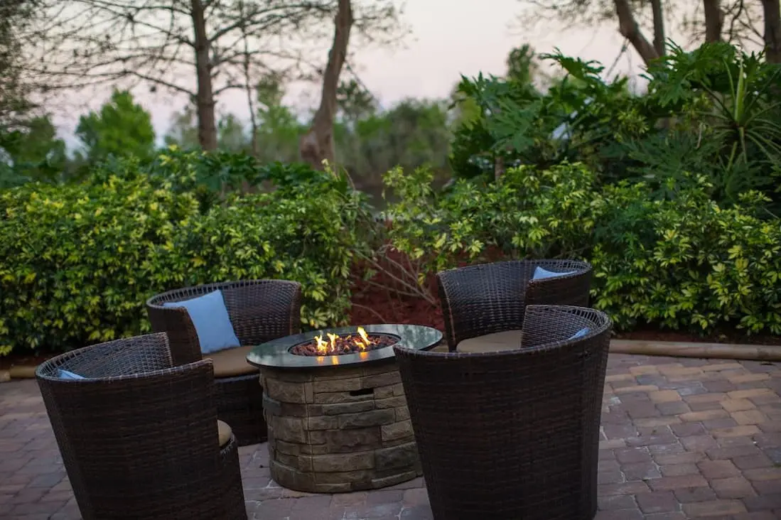 Cozy firepit setting featuring wicker chairs and a stone firepit, nestled in a garden.