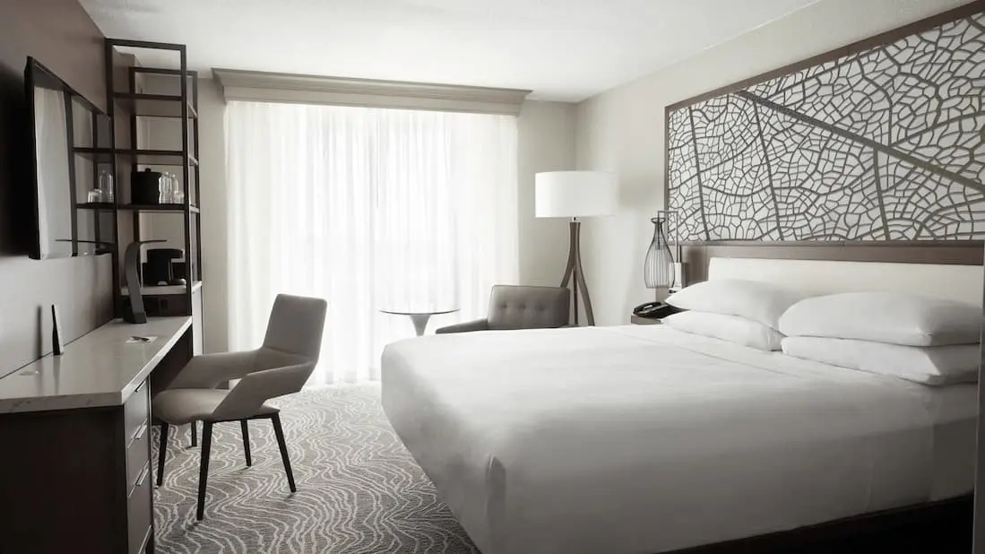 Spacious guest room featuring a king bed, desk, and floor-to-ceiling windows with sheer curtains.
