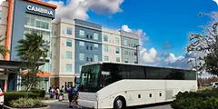 Hotel shuttle bus parked in front of a modern hotel building with palm trees and guests nearby.