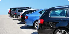 Row of parked cars in an outdoor lot under bright sunlight, near the cruise terminal.
