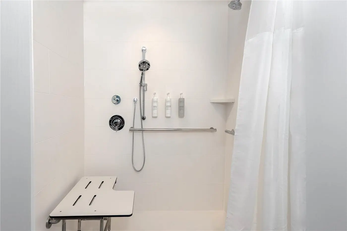 Accessible hotel shower with bench seating, handheld showerhead, and mounted toiletries at Hilton Garden Inn Cape Canaveral near Cocoa Beach.