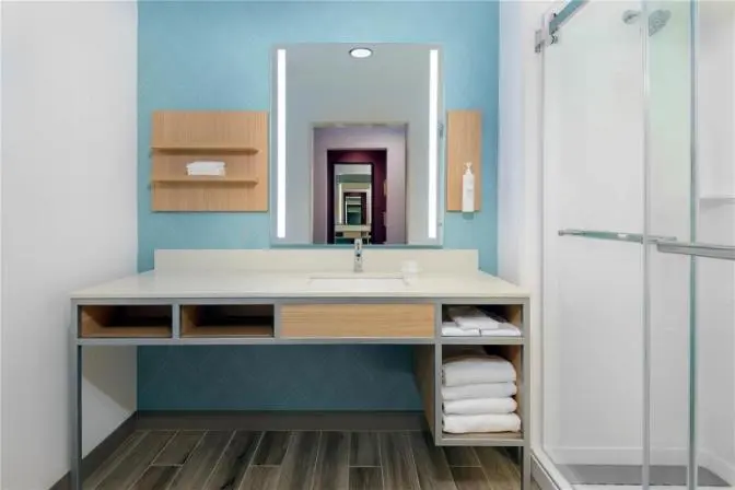 Modern hotel bathroom with illuminated mirror, vanity, and glass-enclosed shower at Hilton Garden Inn Cape Canaveral near Cocoa Beach.