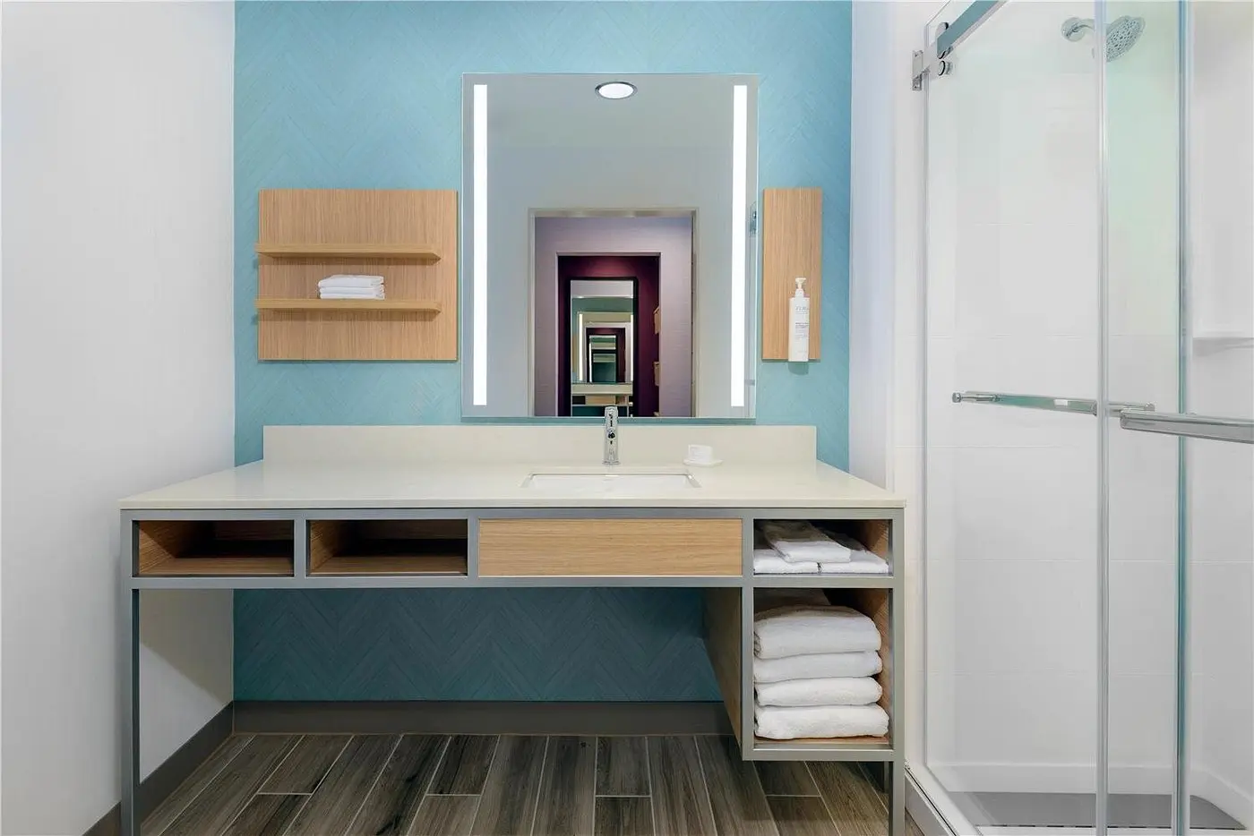Modern hotel bathroom with illuminated mirror, vanity, and glass-enclosed shower at Hilton Garden Inn Cape Canaveral near Cocoa Beach.