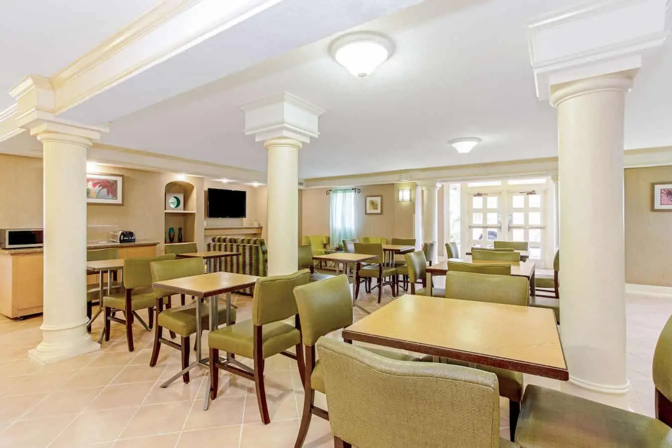 Breakfast seating area with tables and chairs at La Quinta Inn by Wyndham Orlando Airport West.