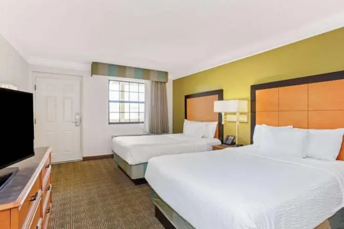 Guest room with two double beds, TV, and workspace at La Quinta Inn by Wyndham Orlando Airport West.