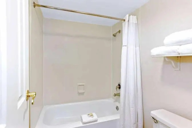 Guest bathroom with bathtub, shower curtain, and fresh towels at La Quinta Inn by Wyndham Orlando Airport West.