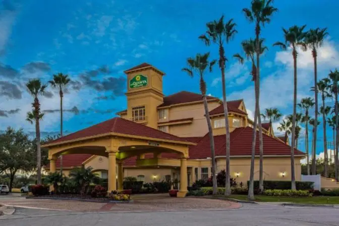 Exterior view of La Quinta Inn & Suites Orlando International Airport Hotel, featuring a grand entrance with tall palm trees displayed against an afternoon sky.