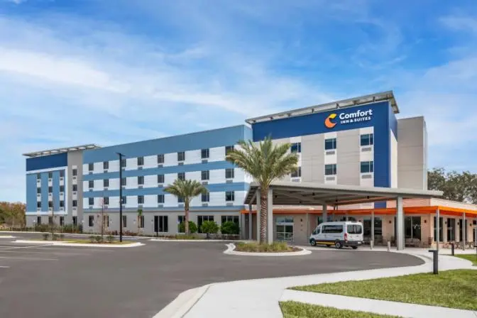 Exterior view of Comfort Inn & Suites Sanford hotel featuring a modern entrance and large palm trees.