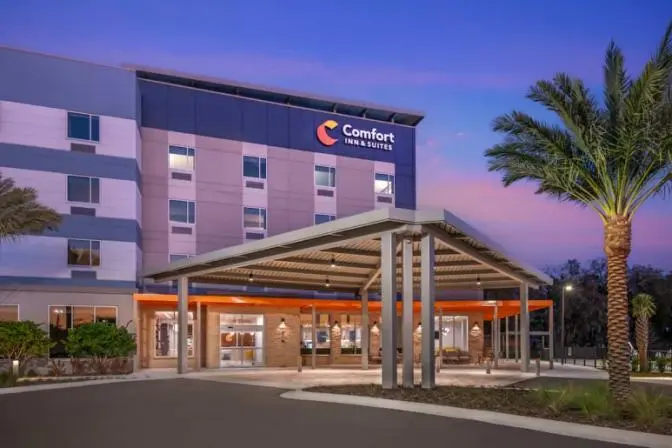 Exterior view of Comfort Inn & Suites Sanford hotel during dusk, featuring a modern entrance and large palm trees.