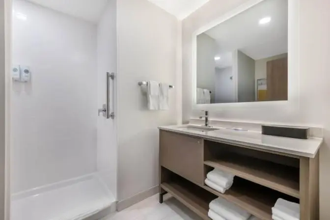 Modern bathroom at Comfort Inn & Suites featuring a wide vanity with a large mirror, and open shelves.