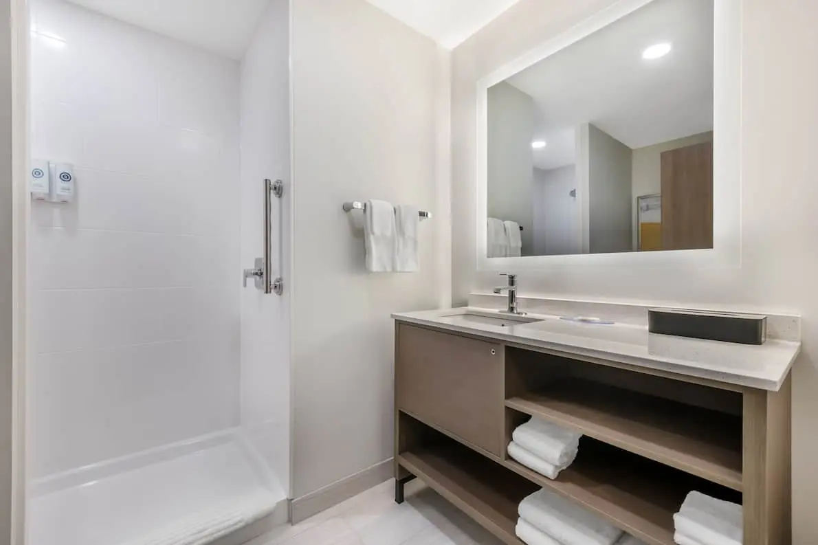 Modern bathroom at Comfort Inn & Suites featuring a wide vanity with a large mirror, and open shelves.