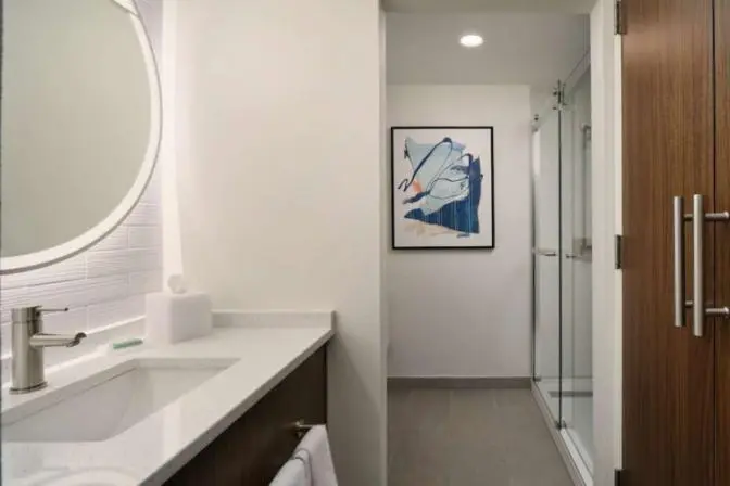 Bathroom at the Courtyard by Marriott featuring a shower with a stand-up sliding glass door, granite countertop with a sink, a large mirror, and neatly arranged towels on a towel rack.