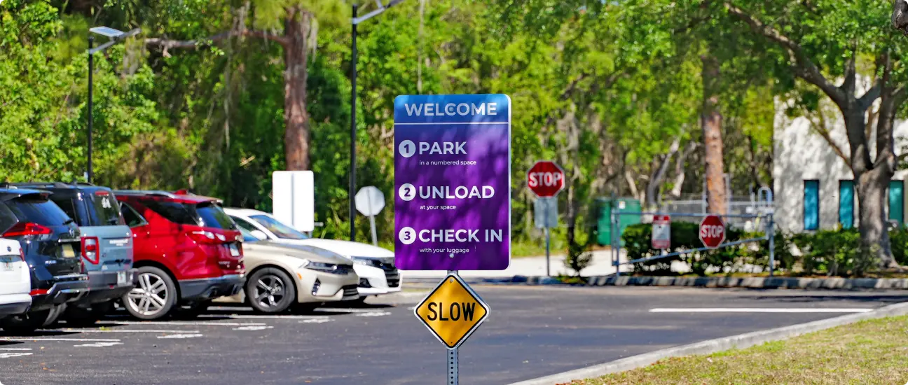 Parking area at Go Port Plaza with a welcome sign outlining steps to park, unload, and check in, surrounded by trees and parked cars.