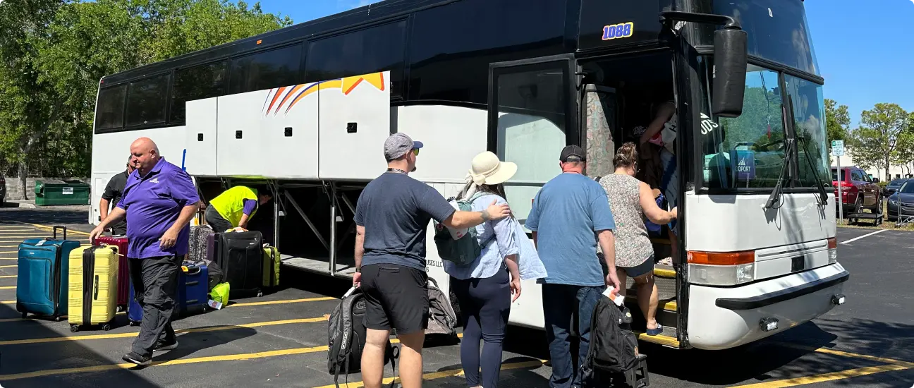Travelers boarding a Go Port shuttle bus with their luggage, assisted by staff, in a parking area on a sunny day.